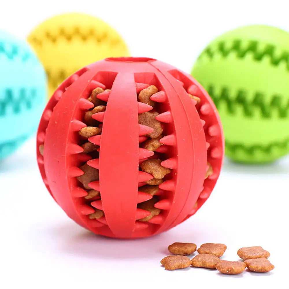 Red dog toy ball with textured surface and small treats inside, surrounded by other colorful toy balls on a white background.