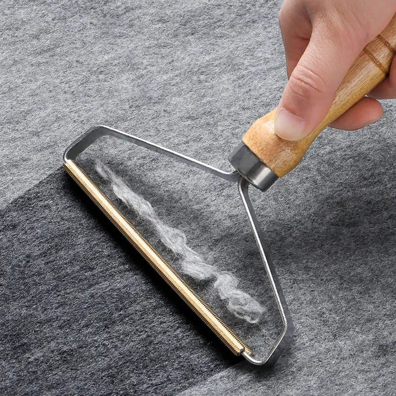 A close-up of a hand holding a lint roller with a light wood handle and metal frame, rolling over gray fabric to show the removal of white lint.